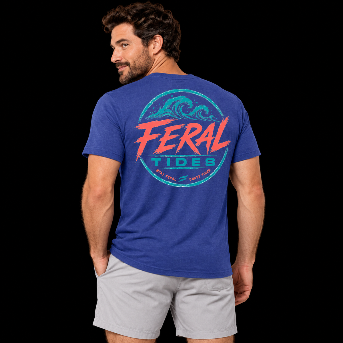 Male model wearing the Deep Blue Feral Tides Tidal Rebel Tee, looking back over left shoulder with one hand in pocket, showing the large coral-and-teal wave graphic on the back against a solid black background.