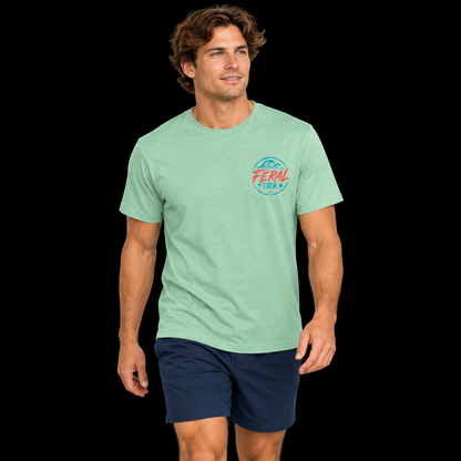 Male model wearing the Heather Neo Mint Feral Tides Tidal Rebel Tee, walking casually with arms relaxed, showing the small coral-and-teal wave logo on the front chest against a solid black background.