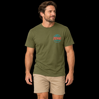 Male model wearing the Military Green Feral Tides Tidal Rebel Tee, walking casually and looking right, showing the small coral-and-teal wave logo on the front chest against a solid black background.
