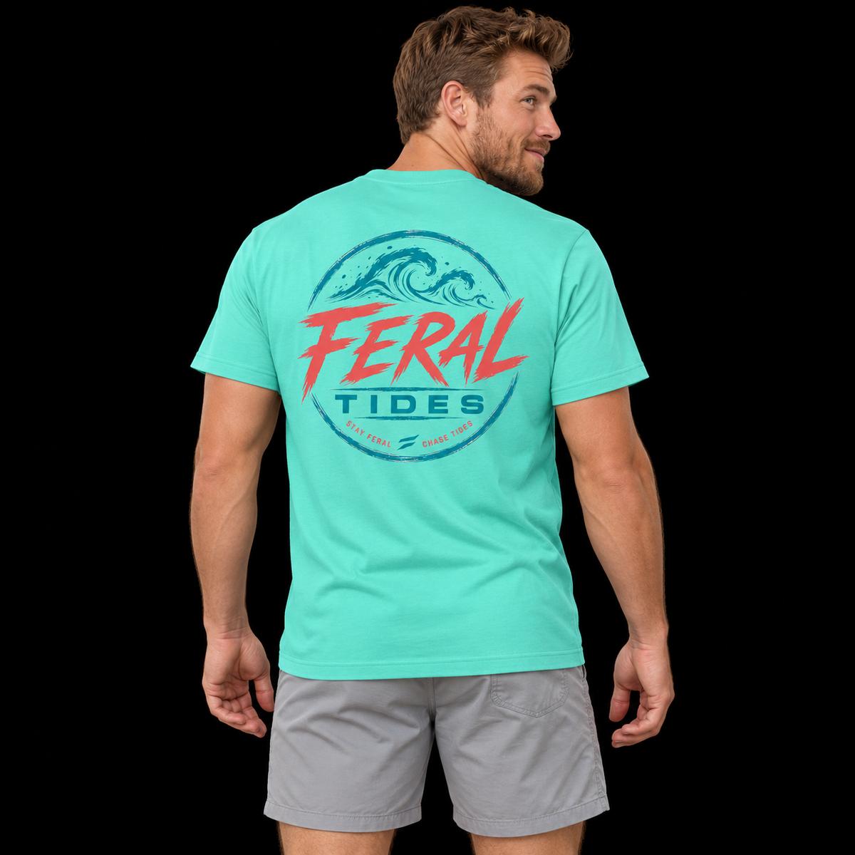 Male model wearing the Mint Feral Tides Tidal Rebel Tee, looking back over right shoulder with arms relaxed, showing the large coral-and-teal wave graphic on the back against a solid black background.
