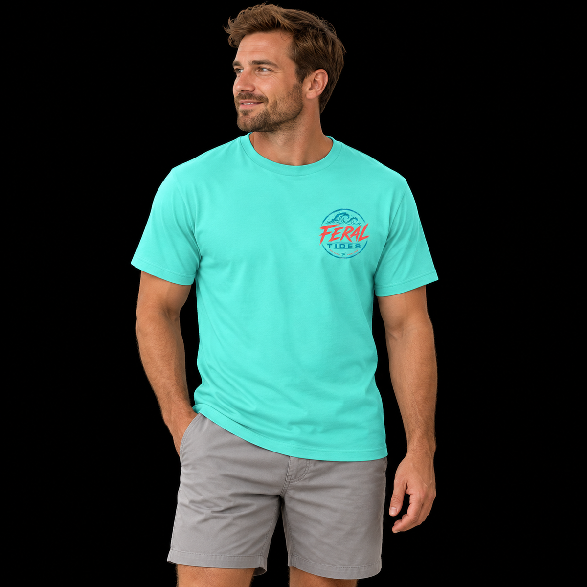 Male model wearing the Mint Feral Tides Tidal Rebel Tee, standing with one hand in pocket and looking left, showing the small coral-and-teal wave logo on the front chest against a solid black background.