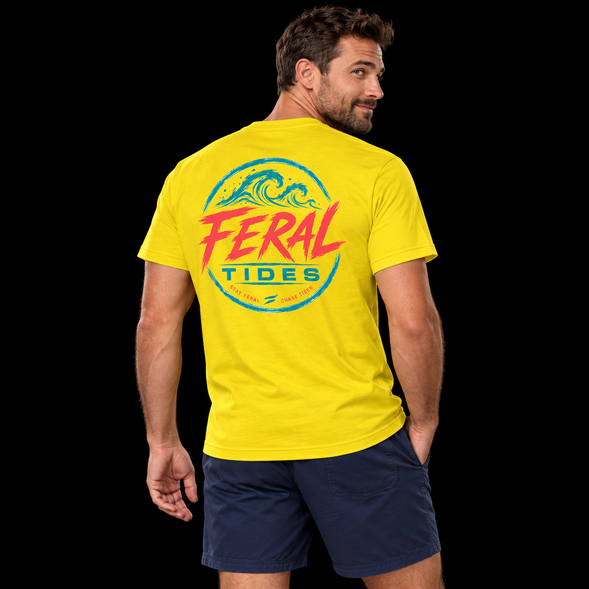 Male model wearing the Sunshine Feral Tides Tidal Rebel Tee, looking back over right shoulder with one hand in pocket, showing the large coral-and-teal wave graphic on the back against a solid black background.